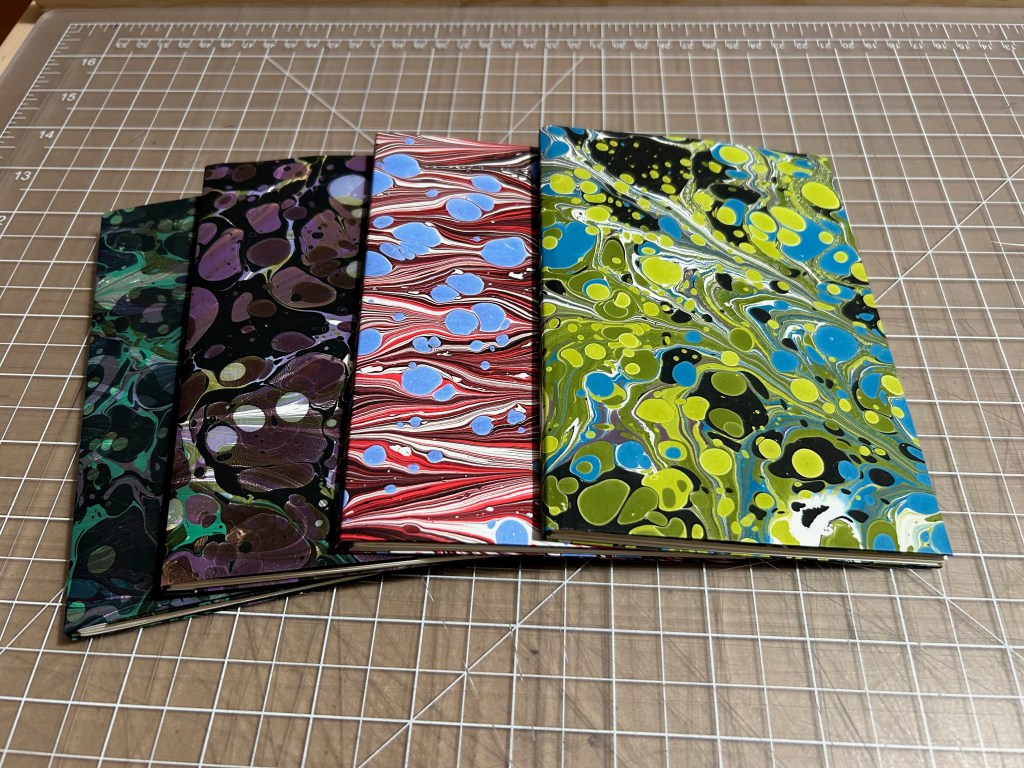Four pocket booklets with distinct marbled covers in greens, purples, reds, and blues.