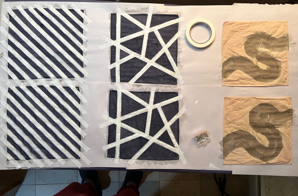 Fabric squares dyed black with white tape lines intersecting throughout. 