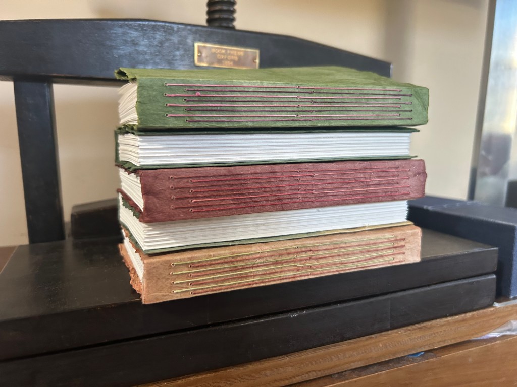 Five, long-stitch, exposed sewing bindings in a stack on a book press.